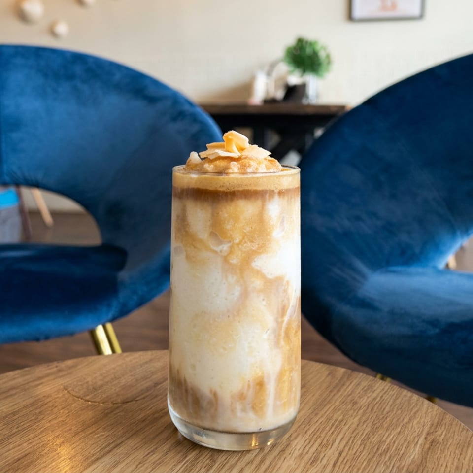 Iced layered coffee topped with whipped cream and almond flakes on a wooden table between blue velvet chairs.